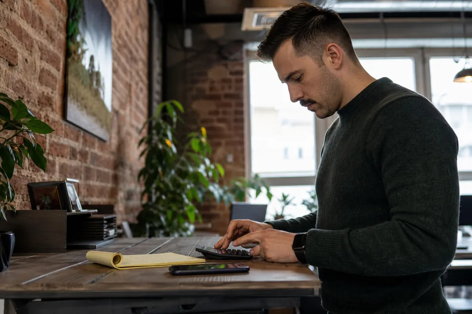 Recruiter at a standing desk working through a hiring budget on a calculator